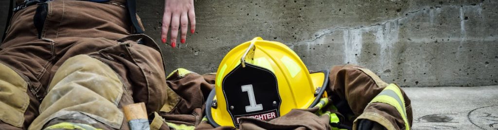 Firewoman taking a break on concrete steps with gear and helmet nearby.