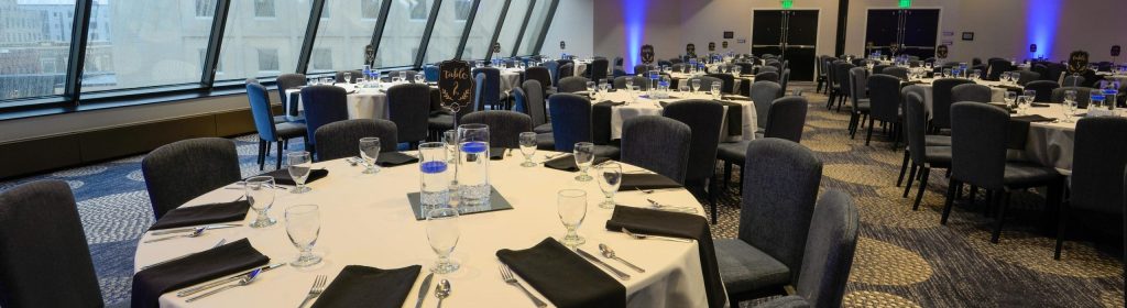 Spacious banquet hall with elegantly set round tables and modern interior lighting.