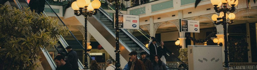 Interior of a vibrant shopping mall with festive holiday decorations and multiple shoppers on escalators.