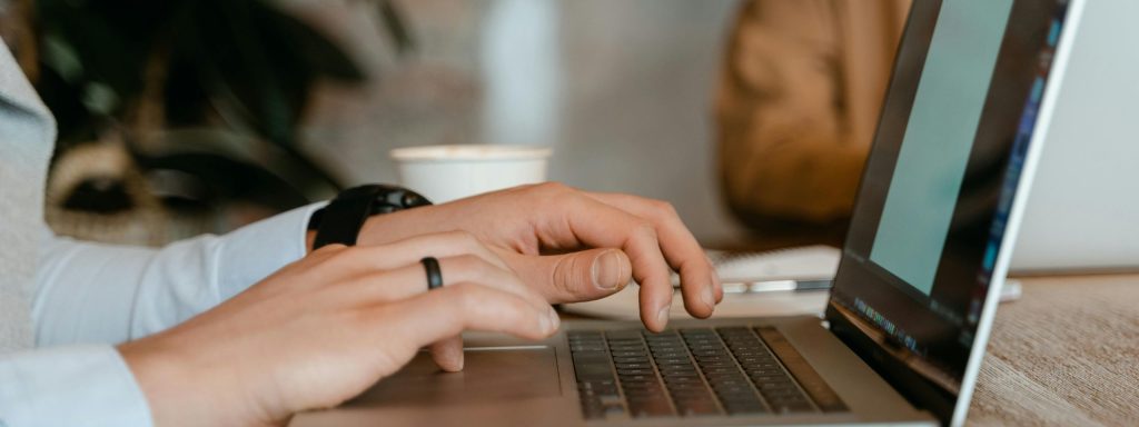 A person typing on a laptop at a wooden table in a modern office setting.